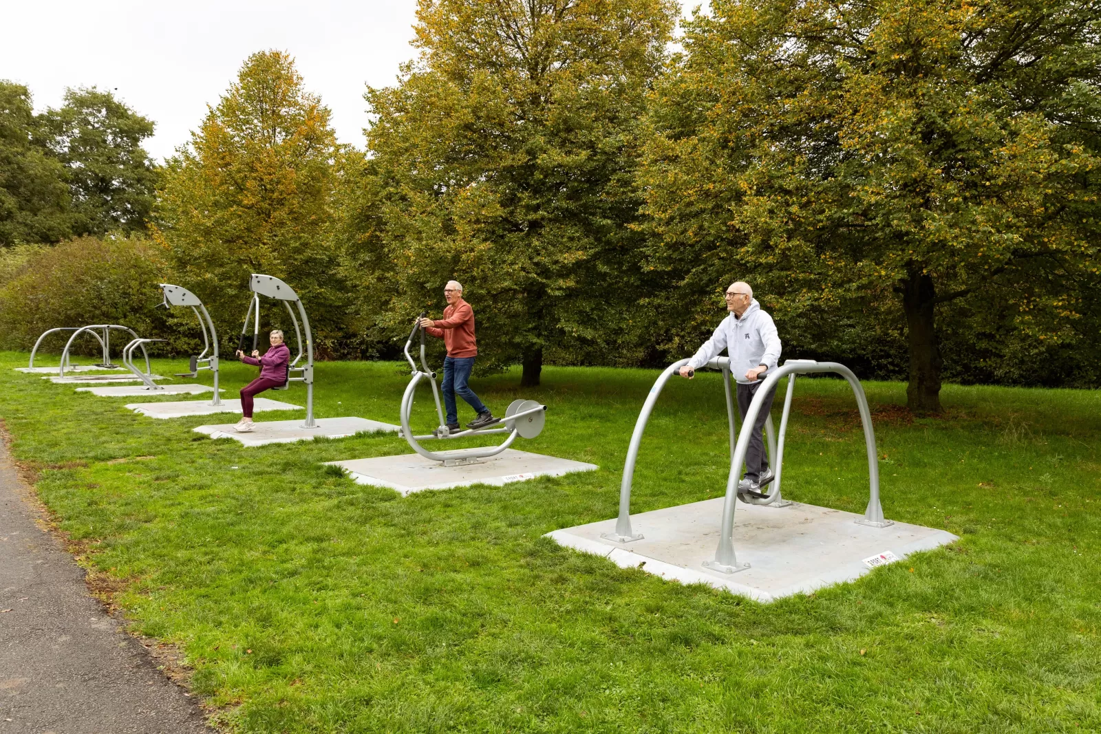 Zeven sporttoestellen met drie sportende mensen naast elkaar in een park